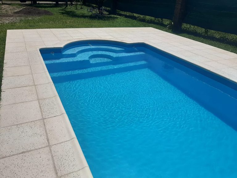 Pileta de fibra de vidrio Moldear línea Arco Romano instalada en el patio de una vivienda, con vereda perimetral y escalera de arco romano